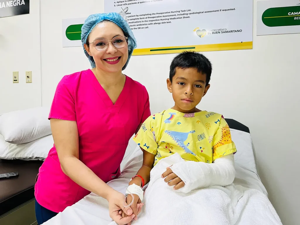 A nurse at Predisan Christian Hospital holds the hand of a young patient sitting in a hospital bed.